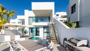 Un patio exterior moderno con piscina, sillones de descanso y una parrilla.