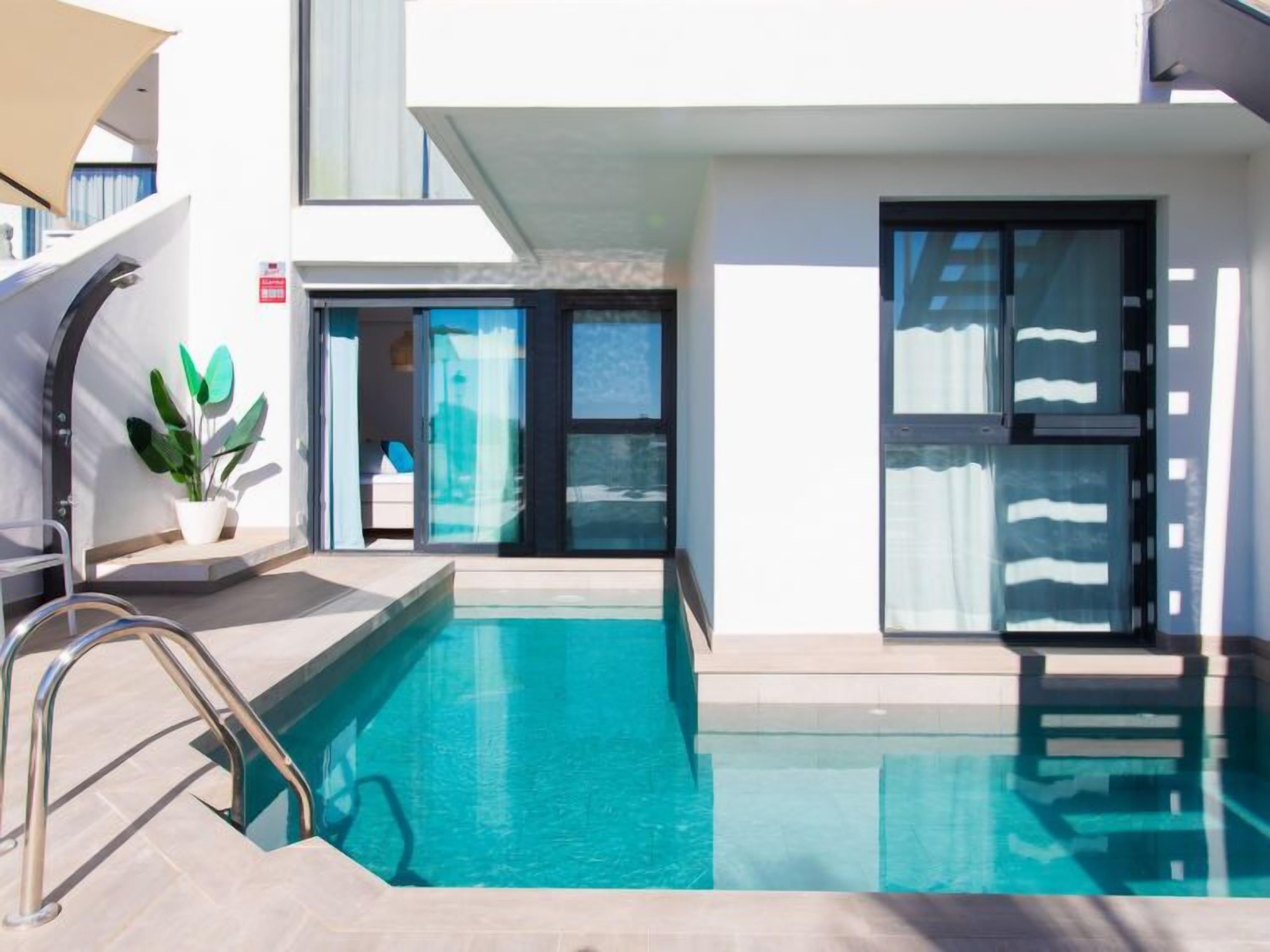 A modern pool area with clear blue water, a metal ladder, and a potted plant.