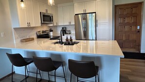 A modern kitchen with white cabinets, stainless steel appliances, a marble island, and three bar stools. - Ultimate Beaver Creek Condo: 3 BED - 3 BATH condo SLEEPS 8 with 6 beds (Avon)