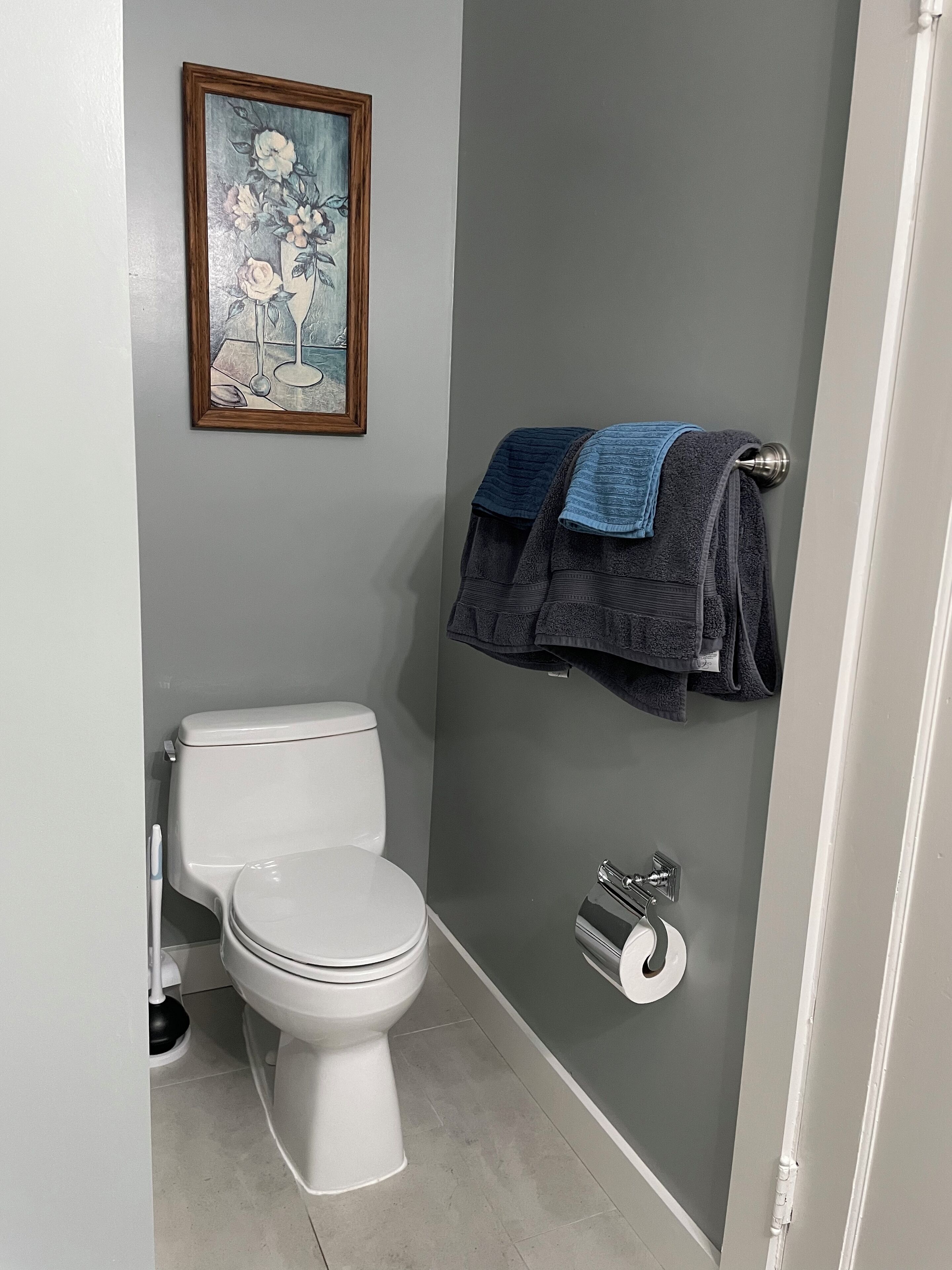 Un bagno con un water, un portascopino, un porta carta igienica e un quadro floreale appeso al muro.