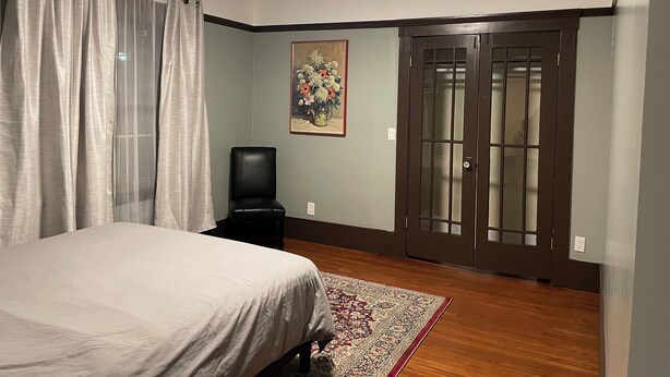 A bedroom with a bed, a chair, a door, and a painting on the wall. - Spacious 1-bedroom in Oakland with AC (Oakland)