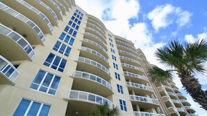 Un hotel de varios pisos con balcones, una palmera y cielo despejado.