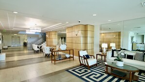 Un lobby espacioso con diseño moderno, que incluye una zona de estar con sofá y sillones, una mesa de centro y una alfombra estampada.