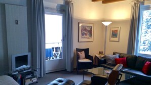 A living room with a television, a sofa, a chair, and a glass coffee table. - WEF Business Apartment (Davos)