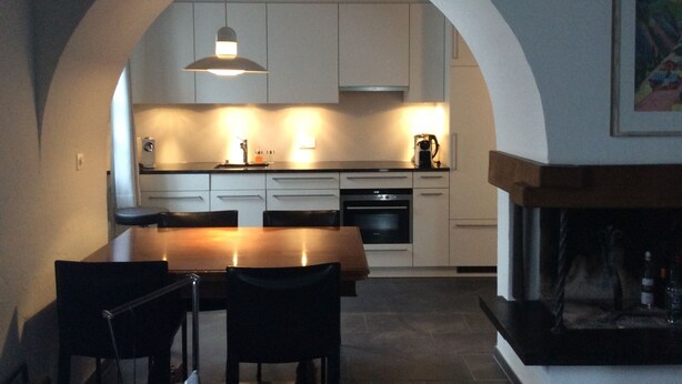 A modern kitchen with white cabinets, a wooden dining table, and black chairs. - WEF Business Apartment (Davos)
