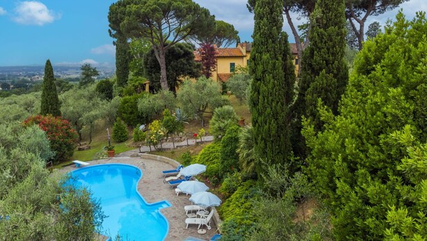 A swimming pool with lounge chairs and umbrellas, surrounded by lush greenery and tall trees. - Beautiful apartment in villa for 10 guests with WIFI, private pool, TV, patio and pets allowed (Monsummano Terme)
