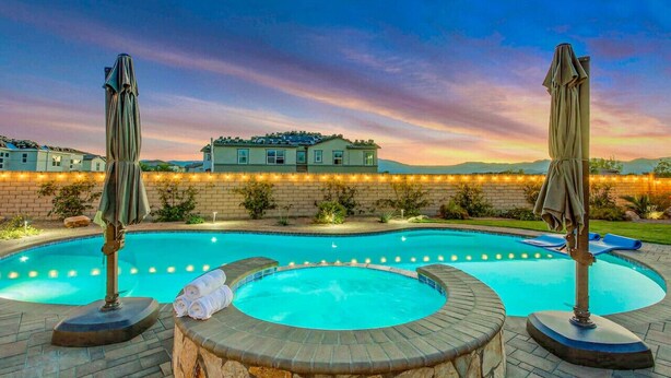 Une piscine avec un jacuzzi, entourée de murs en pierre et agrémentée de deux parasols.