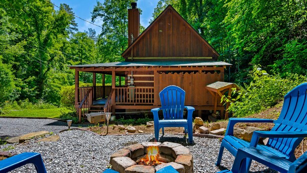 A cabin with a fire pit and two blue Adirondack chairs.