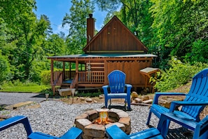 A cabin with a fire pit and two blue Adirondack chairs.