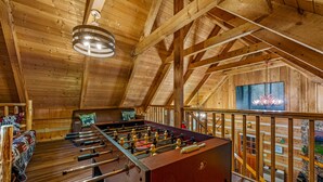 A cozy wooden-floored room with a foosball table, a fireplace, and a large window overlooking a scenic view.