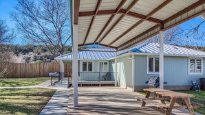 Un patio techado con una mesa de picnic, una parrilla y una casa de techo azul y revestimiento blanco.