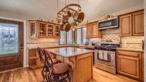 Una cocina con armarios de madera, una isla central, electrodomésticos de acero inoxidable y un colgador para ollas.
