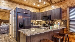 A modern kitchen with dark wood cabinets, stainless steel appliances, a granite countertop, and a built-in island with stools. - ERN805- BEARLY BELIEVE IT! - GREAT LOCATION! CLOSE TO TOWN AND ALL THE ACTION! (Pigeon Forge)