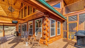 A log cabin with a covered porch, wooden chairs, a grill, and a view of the surrounding landscape. - ERN805- BEARLY BELIEVE IT! - GREAT LOCATION! CLOSE TO TOWN AND ALL THE ACTION! (Pigeon Forge)