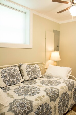 Un dormitorio con cama, ventilador de techo, ventana y lámpara.