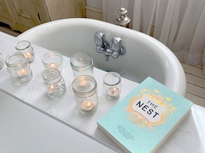 Una bañera blanca con un libro titulado 'The Nest' y varias velas encendidas.