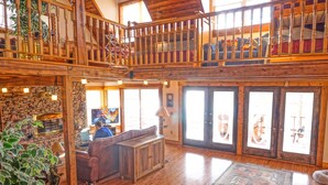 A spacious, wooden-floored living area with a high ceiling, a staircase, and a balcony overlooking the interior. - Norris Lakefront Retreat- Hot Tub, Firepit, Dock. Direct Lake Front. Sleeps 20 (LaFollette)
