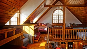 A cozy attic bedroom with wooden beams, a loft bed, and a large window providing natural light. - Norris Lakefront Retreat- Hot Tub, Firepit, Dock. Direct Lake Front. Sleeps 20 (LaFollette)