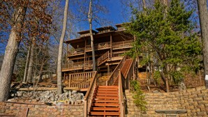 A multi-level wooden cabin with a staircase leading to a balcony, surrounded by trees. - Norris Lakefront Retreat- Hot Tub, Firepit, Dock. Direct Lake Front. Sleeps 20 (LaFollette)