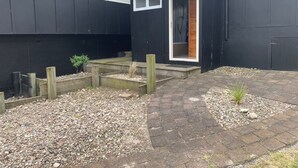 A black building with a wooden door and windows. There is a gravel and stone pathway leading to the door.