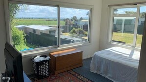A bedroom with a bed, a desk with a computer, a window, and a view of the outside.