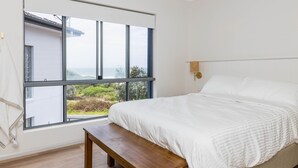 A bedroom with a large window, a bed, a bench, and a wall-mounted lamp. - Tide at Blueys Beach - Dog Friendly Beachfront (Blueys Beach)