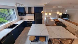 A modern kitchen with a marble island, built-in appliances, and a large window offering a view of greenery. - Tide at Blueys Beach - Dog Friendly Beachfront (Blueys Beach)