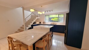A modern kitchen with a marble countertop, wooden chairs, and a staircase leading to an upper level. - Tide at Blueys Beach - Dog Friendly Beachfront (Blueys Beach)
