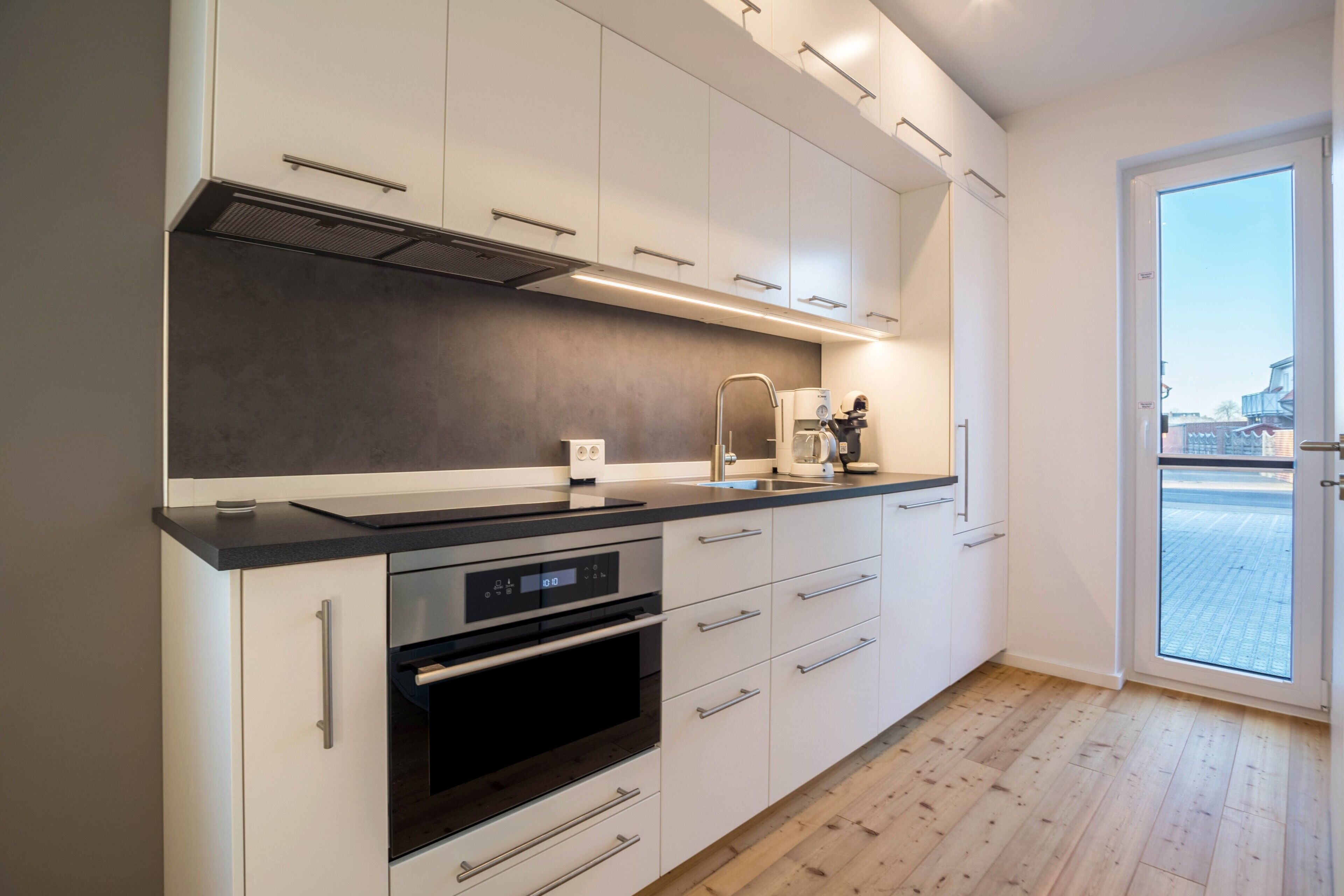 A modern kitchen with white cabinets, a black countertop, and a built-in oven.