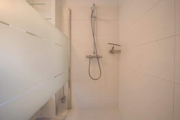 A shower with a handheld showerhead and a wall-mounted faucet in a tiled bathroom.