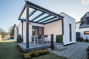 Une maison moderne dotée d’un patio couvert, d’un coin repas et d’un petit jardin.