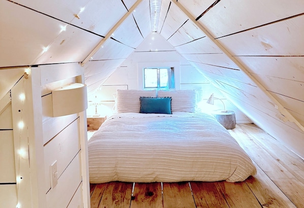 A bedroom with a sloped ceiling, a bed with striped bedding, a window, and a bedside lamp.