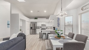 Una cocina moderna con armarios blancos, un refrigerador de acero inoxidable y un comedor con mesa blanca y sillas grises.