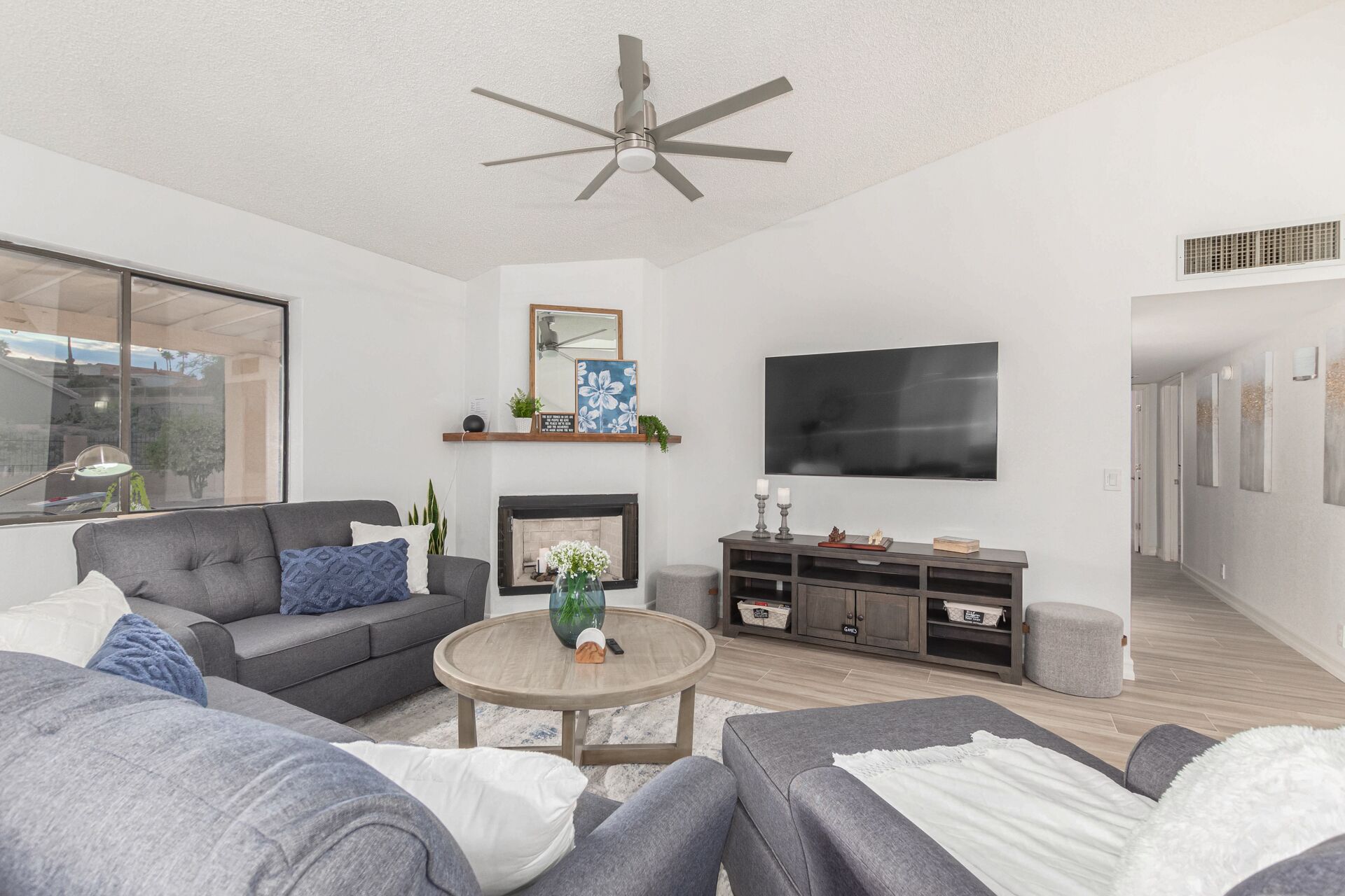 Ein modernes Wohnzimmer mit grauem Sofa, einem runden Couchtisch, einem Kamin und einem Deckenventilator.