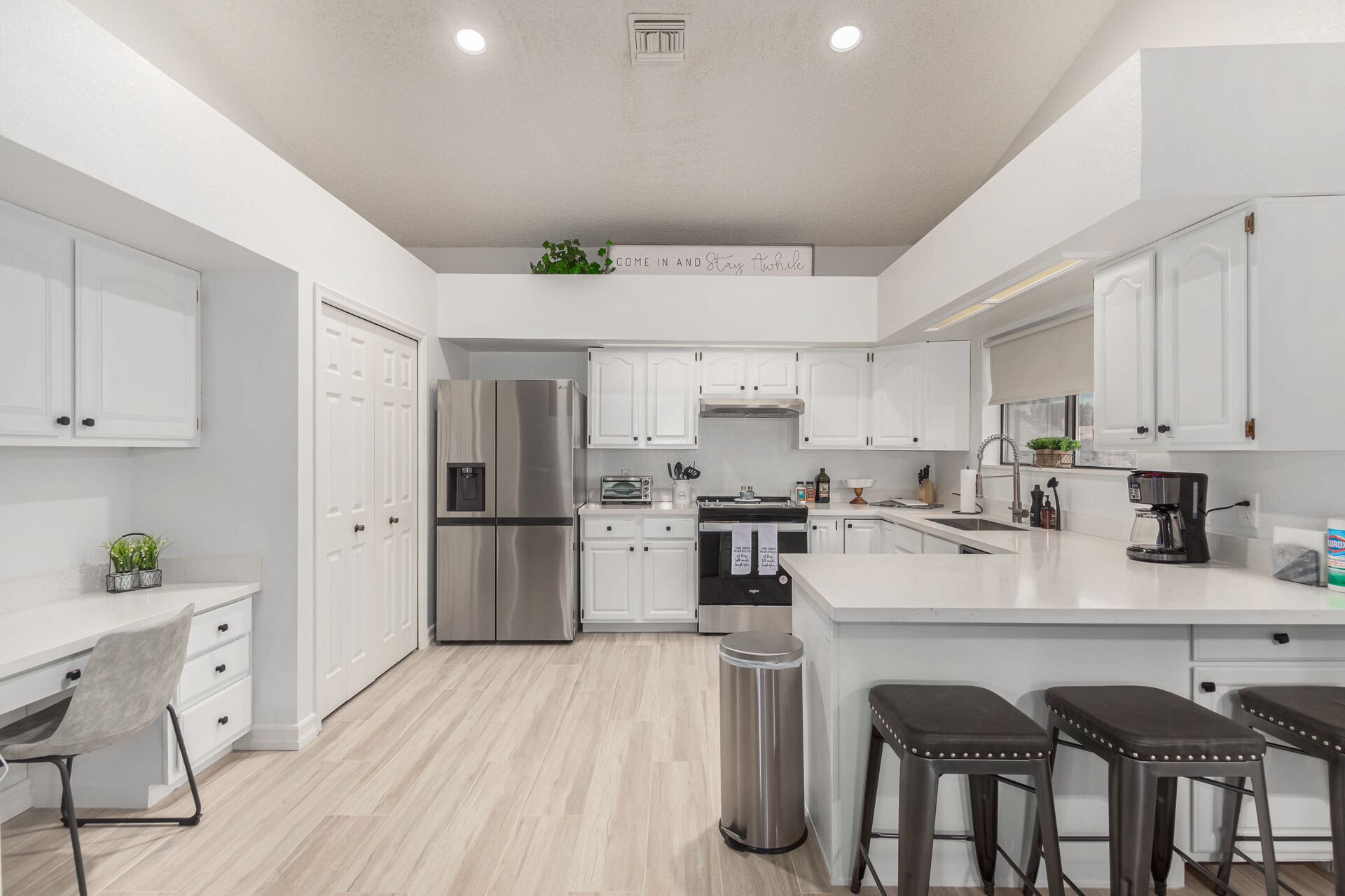 A modern kitchen with white cabinetry, stainless steel appliances, a central island, and a trash can.