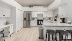 Una cocina moderna con armarios blancos, electrodomésticos de acero inoxidable, una isla central y un cubo de basura.