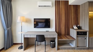 A hotel room with a desk, chair, TV, air conditioning unit, and a minibar. - Veno Hotel (George Town)