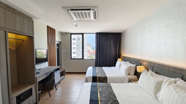 A hotel room with two beds, a desk, a TV, and a view of buildings. - Veno Hotel (George Town)