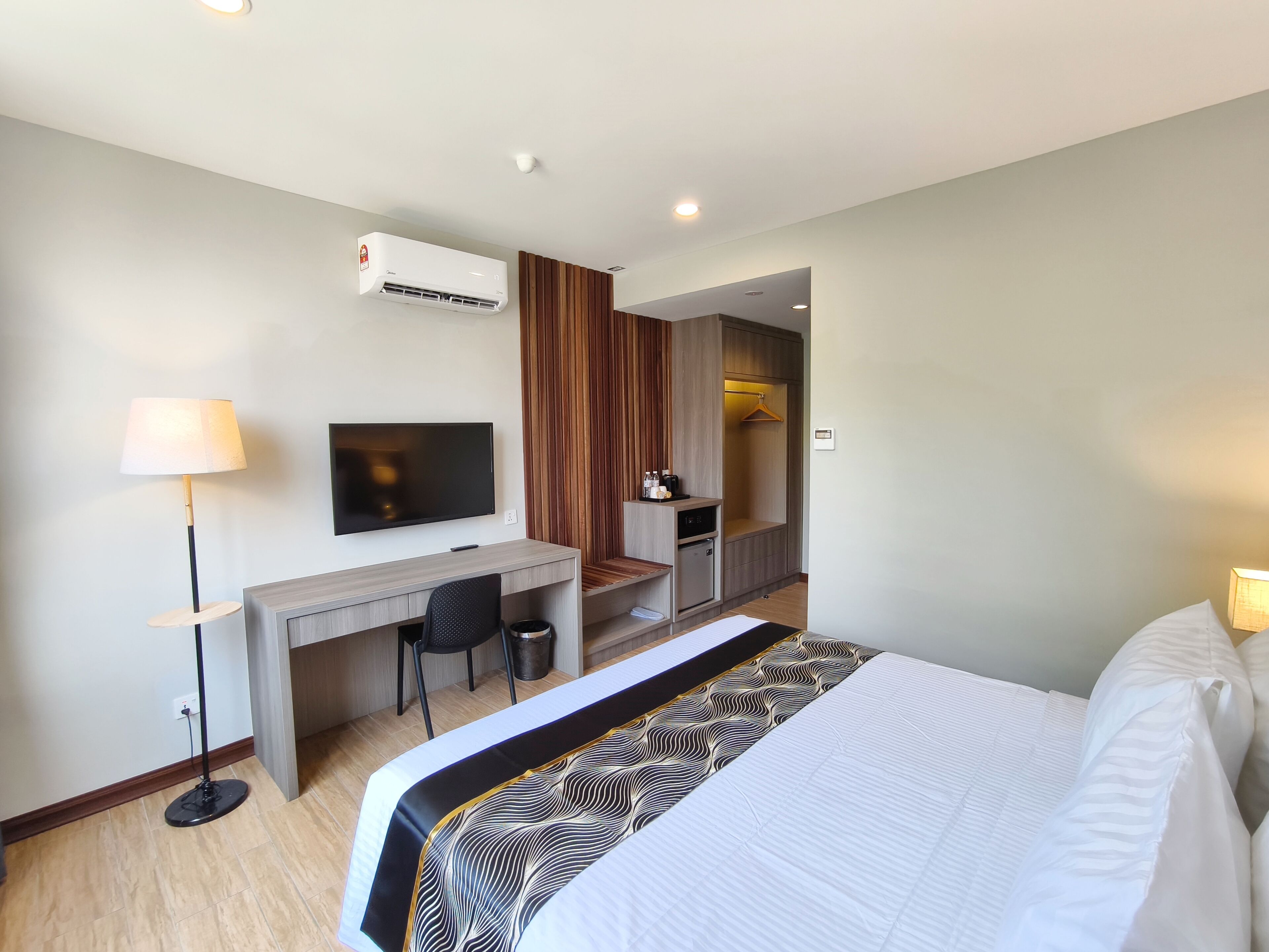 A hotel room with a bed, a desk with a TV, a wardrobe, and a small kitchenette.