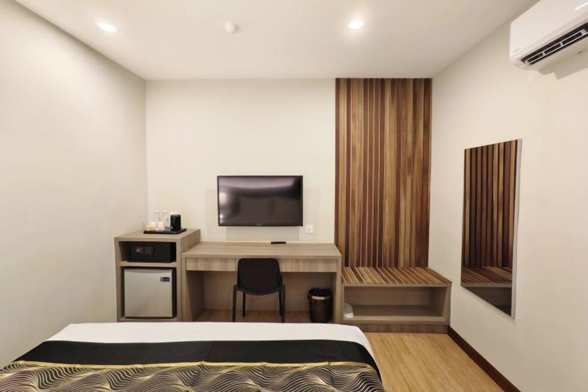 Ett hotellrum med en säng, ett skrivbord med en tv, ett litet kylskåp och en väggpanel i trä.