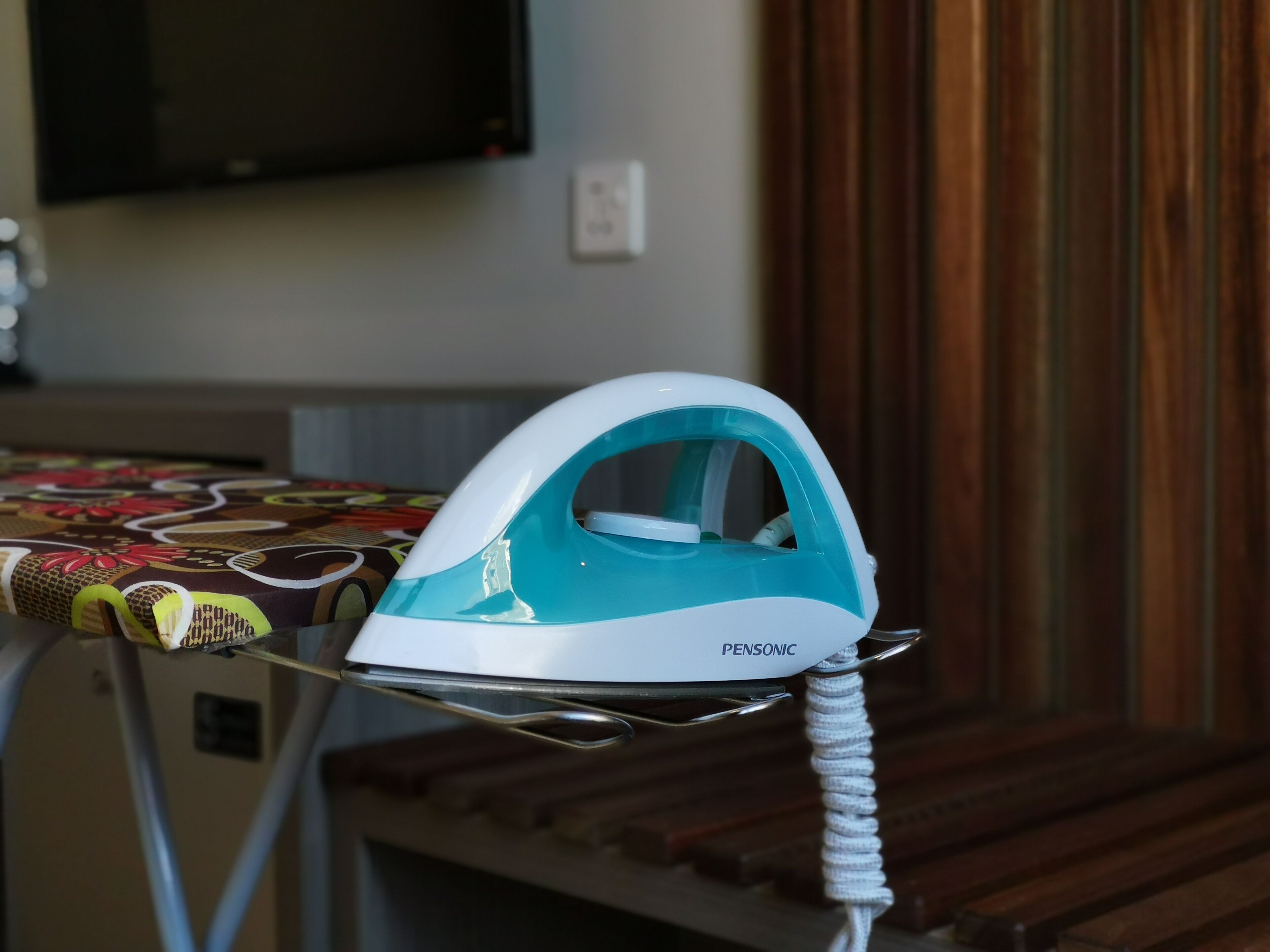 A white and teal iron on an ironing board with a floral tablecloth.