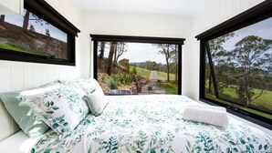 Un dormitorio con una cama grande, vista a un paisaje rural y una pequeña construcción de madera al fondo.