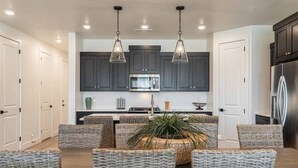 A modern kitchen with dark cabinets, a stainless steel refrigerator, and a central island with seating. - Desert Azul by RedAwning (St. George)
