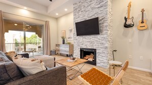 A modern living room with a fireplace, a flat-screen TV, and two guitars on the wall. - Eucalyptus by AvantStay | Stunning Scottsdale Home w/ Communal Pool & Hot Tub (Scottsdale)