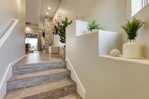 Eine Holztreppe führt zu einem Wohnbereich mit einer Steinwand, einem Kamin und Blick in den Essbereich.