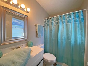 A bathroom with a white sink, a mirror with lights, a toilet, and a shower curtain with a blue pattern. - Elizabeth Rd House by Palmetto Vacations (Myrtle Beach)