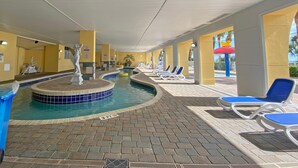 An indoor swimming pool with a fountain, lounge chairs, and a tiled floor. - Camelot by the Sea by Palmetto Vacations (Myrtle Beach)