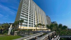 A high-rise hotel with multiple balconies, a rooftop pool, and a wooden boardwalk leading to the pool area. - Camelot by the Sea by Palmetto Vacations (Myrtle Beach)