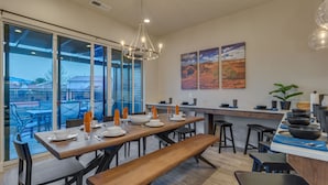 A modern kitchen with a large dining table, bar area, and large windows offering a view of the outdoors. - Snow Canyon Oasis, Ocotillo 42, Large Private Pool and Hot Tub, 2 Firepits, 2 PlayStations (Santa Clara)
