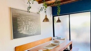 Un comedor con mesa de madera, banco, lámparas colgantes y un cuadro grande en la pared.